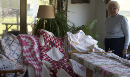 Interviewee Juanita Shockey Harris stands before her family's heirloom quilts.